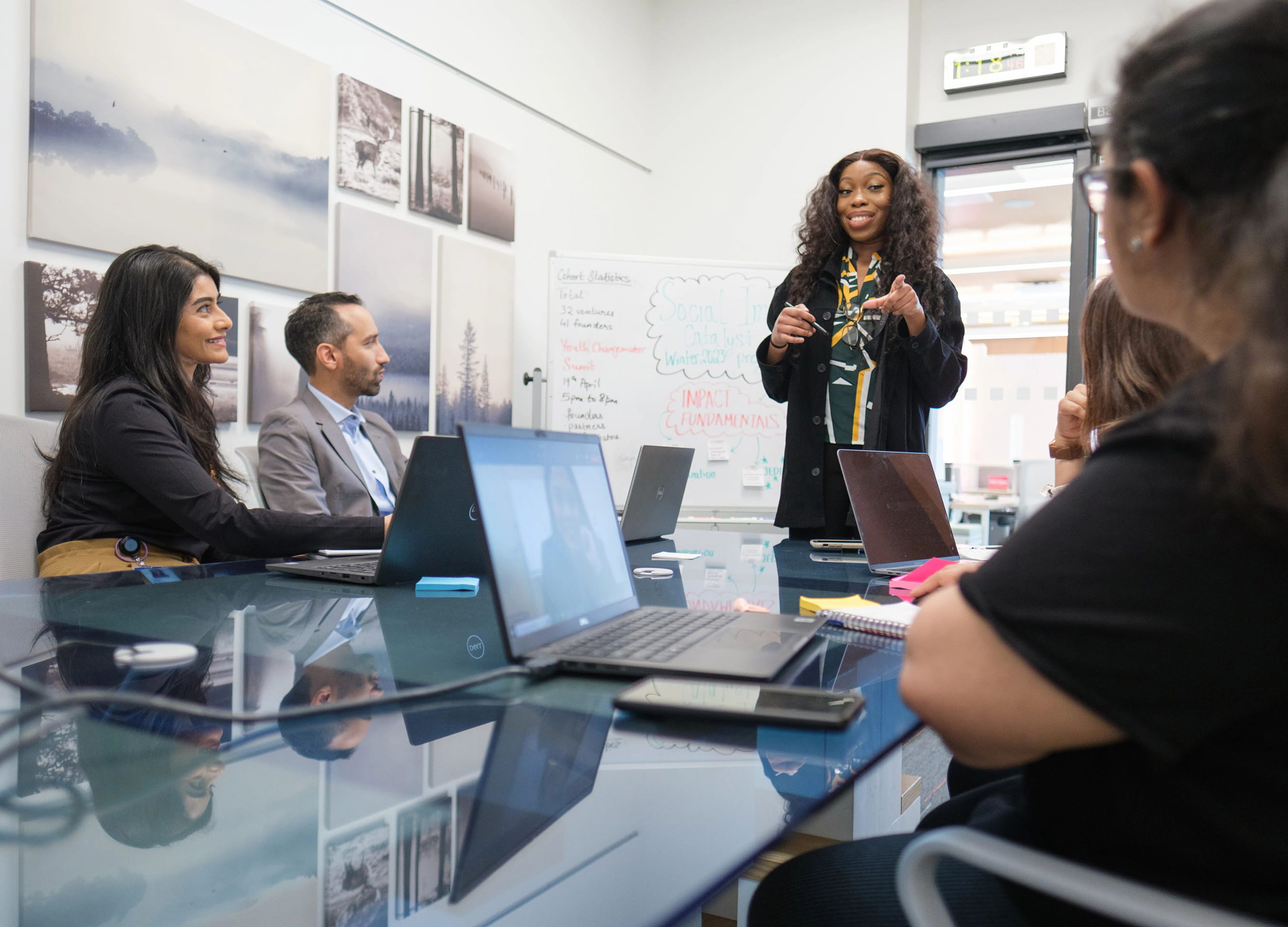 Person standing at a whiteboard presenting to a group of people seated around a table